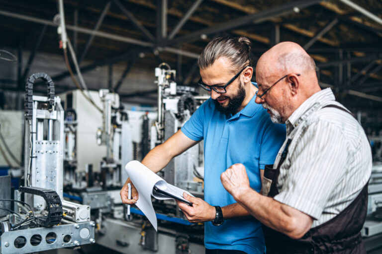 Zwei Industriemechaniker stehen an den Maschinen und schauen die Unterlagen durch